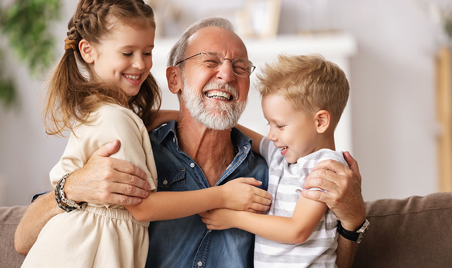 Cheerful aged man smiling and embracing cute boy and girl while resting easy after selling his house for cash